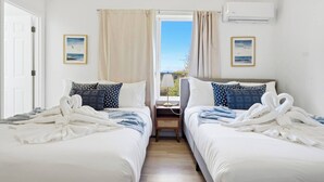 A hotel room with two beds, a window with curtains, a bedside table with a lamp, and an air conditioning unit. - Bright 3BR/2BA Retreat Near UW & Northgate Station (Seattle)