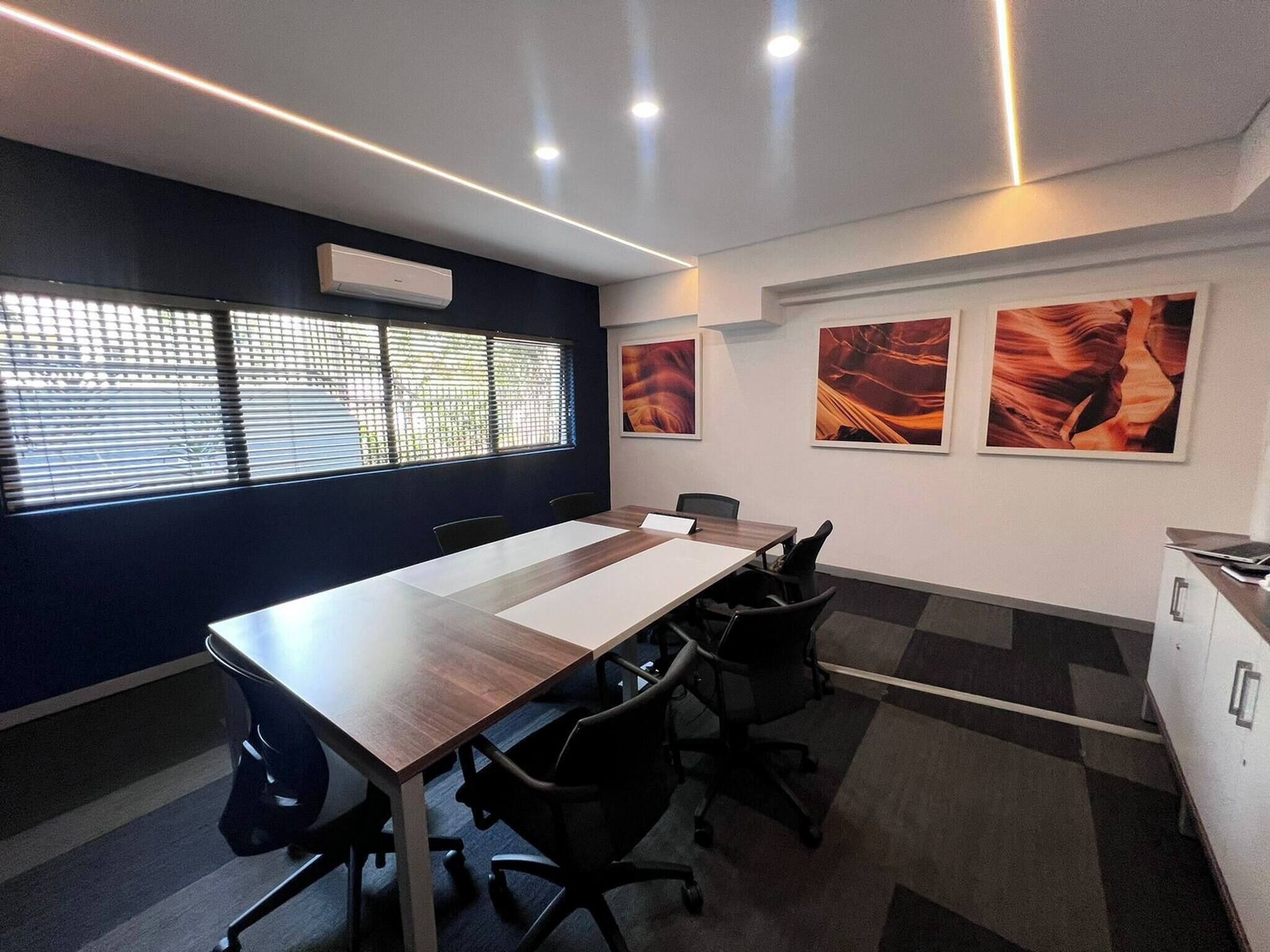 A conference room with a long table, chairs, a whiteboard, and a window with blinds.