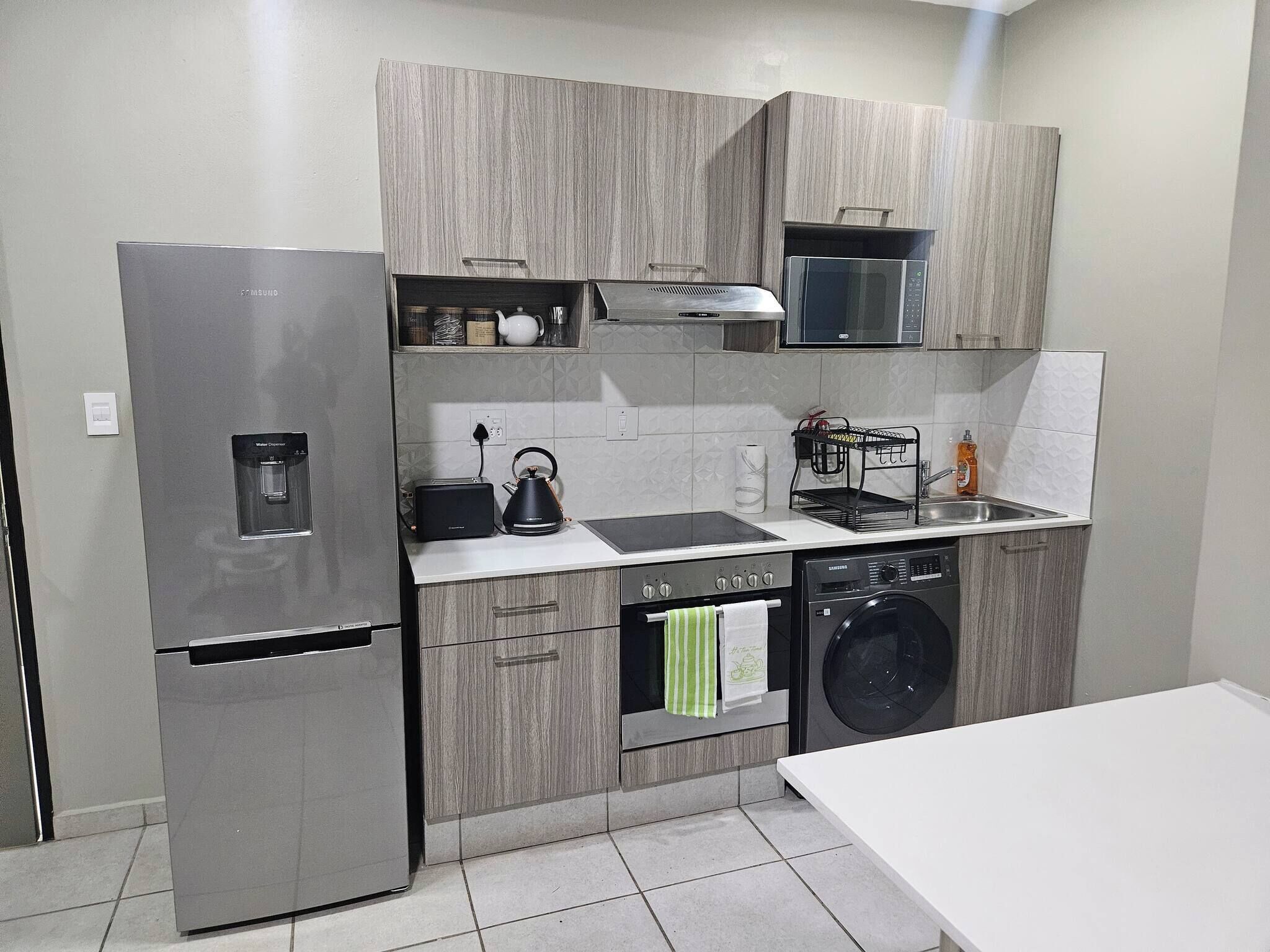 A modern kitchen with a stainless steel refrigerator, a built-in microwave, a dishwasher, and a washing machine.