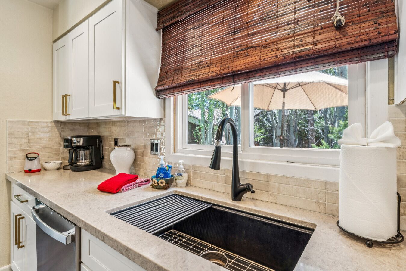A kitchen with white cabinets, a black faucet, a window with a view, and a dish drying rack.