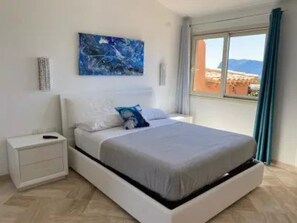 A bedroom with a bed, a nightstand, a wall-mounted artwork, and a window with curtains. - EXCLUSIVE SHERDEN (Golfo Aranci)
