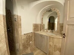 A bathroom with a tiled floor, a sink, a mirror, and a shower area. - EXCLUSIVE SHERDEN (Golfo Aranci)