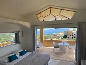A bedroom with a bed, a view of the sea, and a balcony with chairs. - EXCLUSIVE SHERDEN (Golfo Aranci)