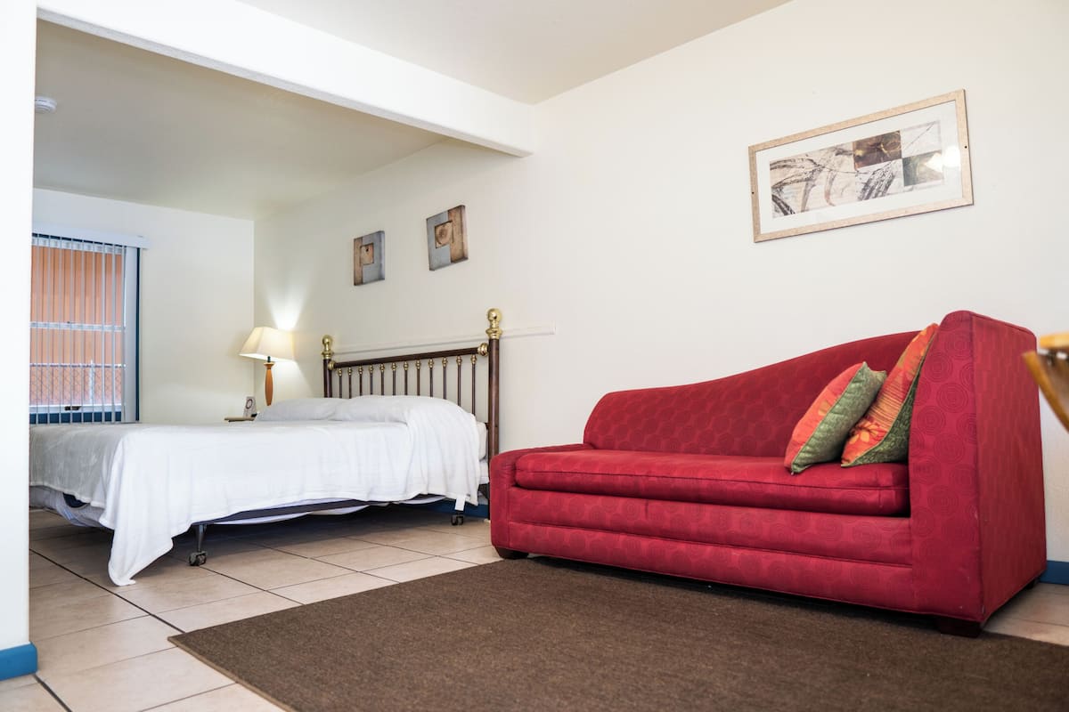 A room with a bed, a red sofa, a lamp, and a framed picture on the wall.