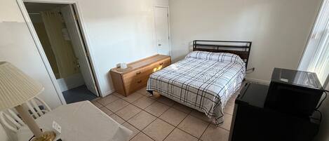A bedroom with a bed, a desk, a chair, a ceiling fan, a TV, and a window.