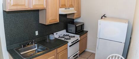 A compact kitchen with a sink, stove, microwave, and refrigerator.