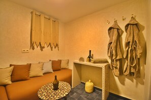 Una habitación acogedora con un sofá, una pequeña mesa redonda, una botella, una cesta tejida y un perchero en la pared.