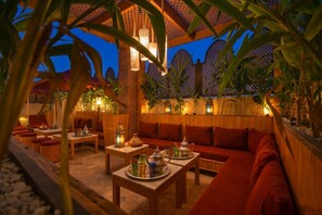 Un espacio al aire libre con mobiliario de madera, mesas con teteras y una pared de madera con diseño de celosía.