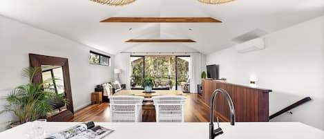 Una cocina moderna con encimera blanca, lavamanos negro y una zona de comedor con sillas de mimbre blanco.
