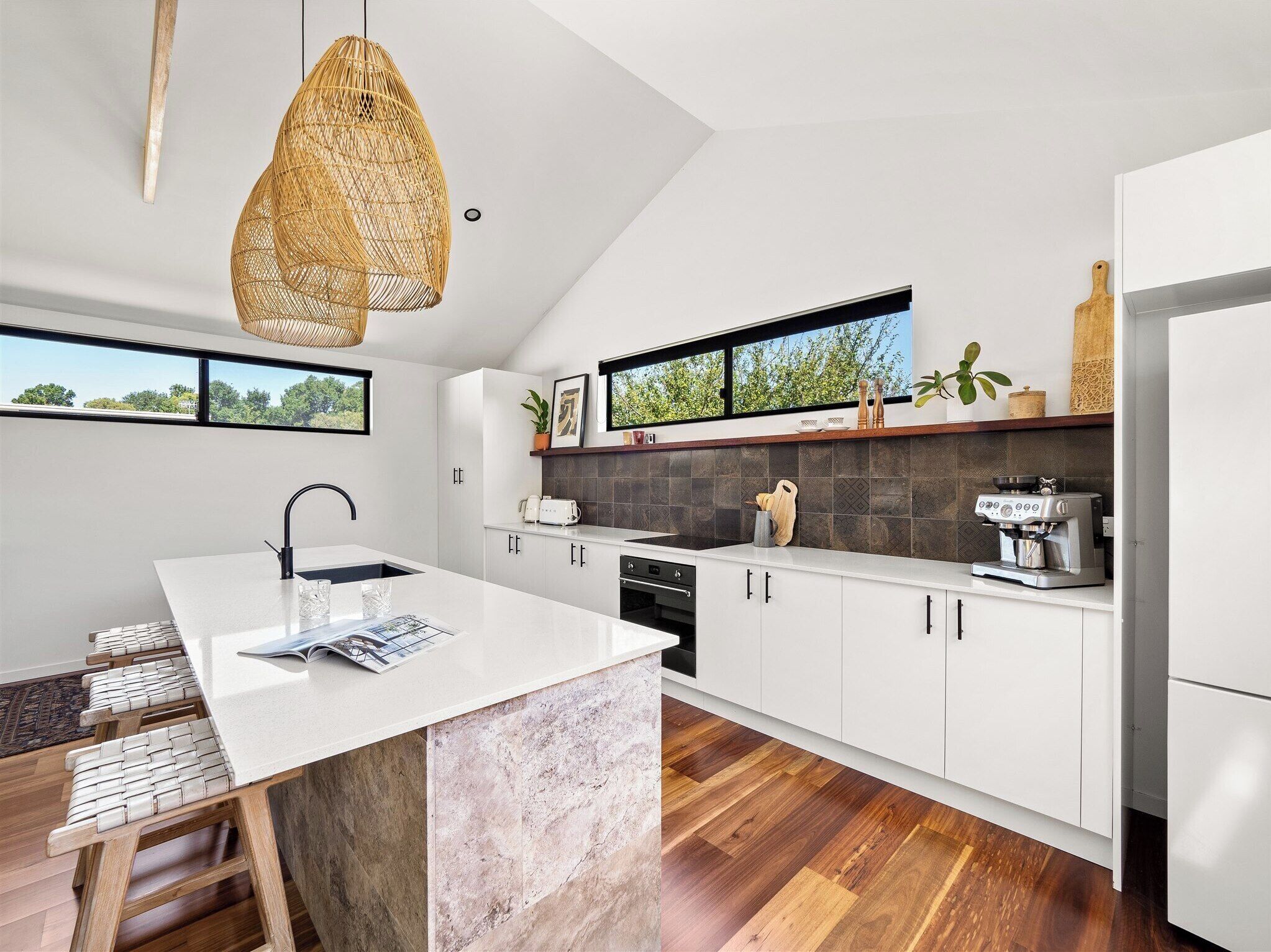 Una cocina moderna con armarios blancos, una isla central, una lámpara colgante y vistas por la ventana.