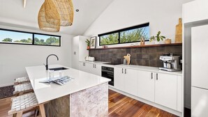 Una cucina moderna con mobili bianchi, un'isola centrale, un lampadario a sospensione e vista dalla finestra.
