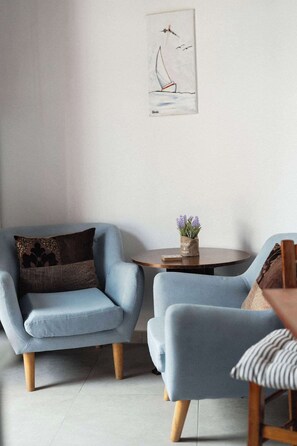 Ein Wohnzimmer mit zwei hellblauen Sesseln, einem kleinen runden Tisch mit Blumenvase und einem an der Wand hängenden Gemälde eines Segelboots.