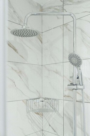 Eine Dusche mit Handbrause und Kopfbrause, einer transparenten Duschwanne und einer gefliesten Wand mit Marmormuster.