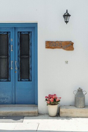 A blue door with a number '2' above it, a wooden sign with '10km' written on it, a potted plant with pink flowers, and a metal container. - Charming 2BR Village Getaway Near the Beach (Agios Theodoros Larnakas)