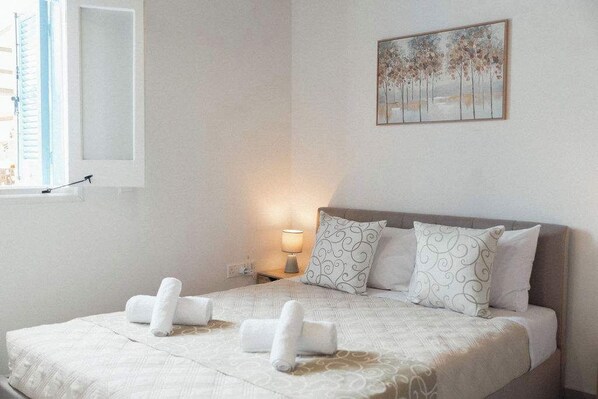 A bedroom with a bed, pillows, a nightstand, a lamp, and a painting on the wall. - Charming 2BR Village Getaway Near the Beach (Agios Theodoros Larnakas)