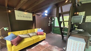 A yellow sofa with pillows, a wooden desk with a computer, a leather rug, and a sign on the wall.
