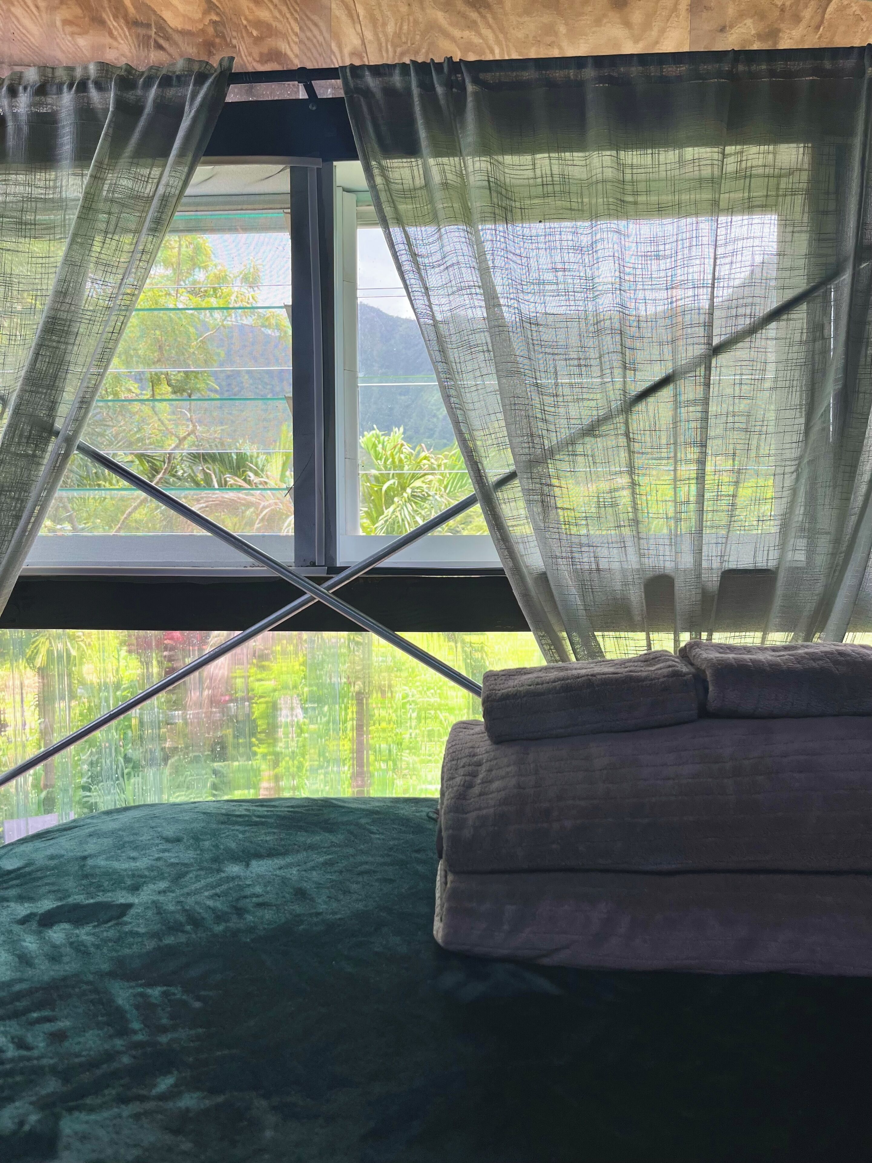Quarto com cama, janela com cortinas e vista para o verde lá fora.