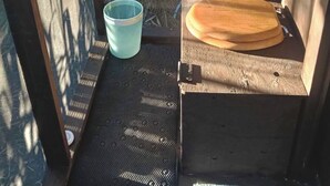 A balcony with a metal grill, a wooden table with a bowl, and a blue bucket.
