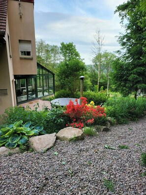 Ein modernes Gebäude mit Glasfassade, ein Garten mit verschiedenen Pflanzen und Blumen sowie ein Kiesweg.