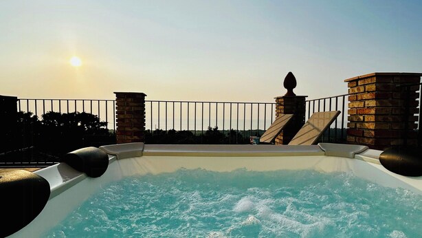 Un jacuzzi con vista al atardecer, una pared de piedra y una barandilla metálica.