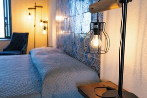 Una habitación de hotel con cama, mesita de noche, lámpara y pared con estampado.
