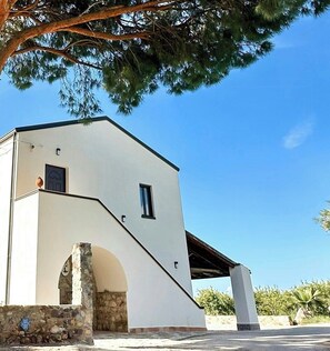 Un edificio de fachada blanca, un arco de piedra y un cielo azul despejado.