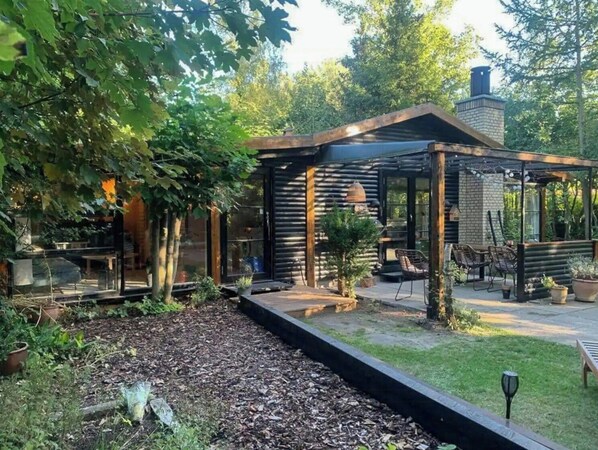 Ein modernes Blockhaus mit überdachter Terrasse, Sitzgelegenheiten im Freien und einem Garten.