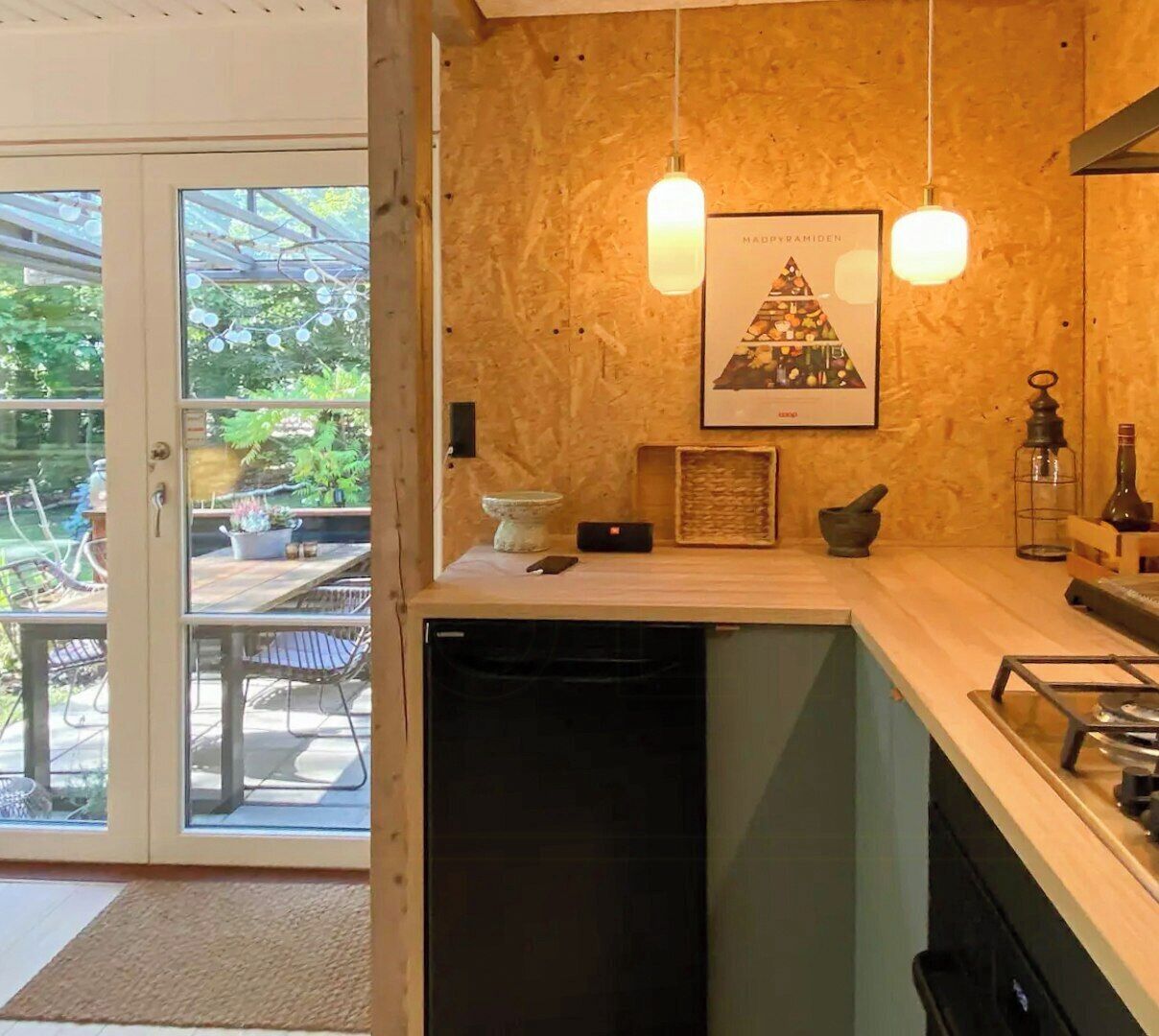 Cozinha moderna com armários de madeira, iluminação pendente e vista para um pátio externo através de portas de vidro.