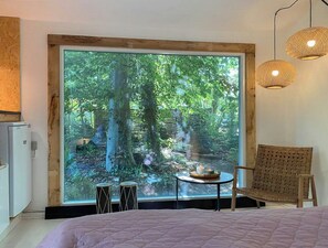 A bedroom with a large window, a bed, a chair, a small table with candles, and a wall-mounted light fixture. - House in Skæring near city and nature (Egå)