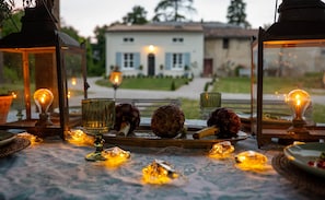 Ein Tisch gedeckt mit Kerzen, Laternen und Artischocken, im Hintergrund ein Haus.