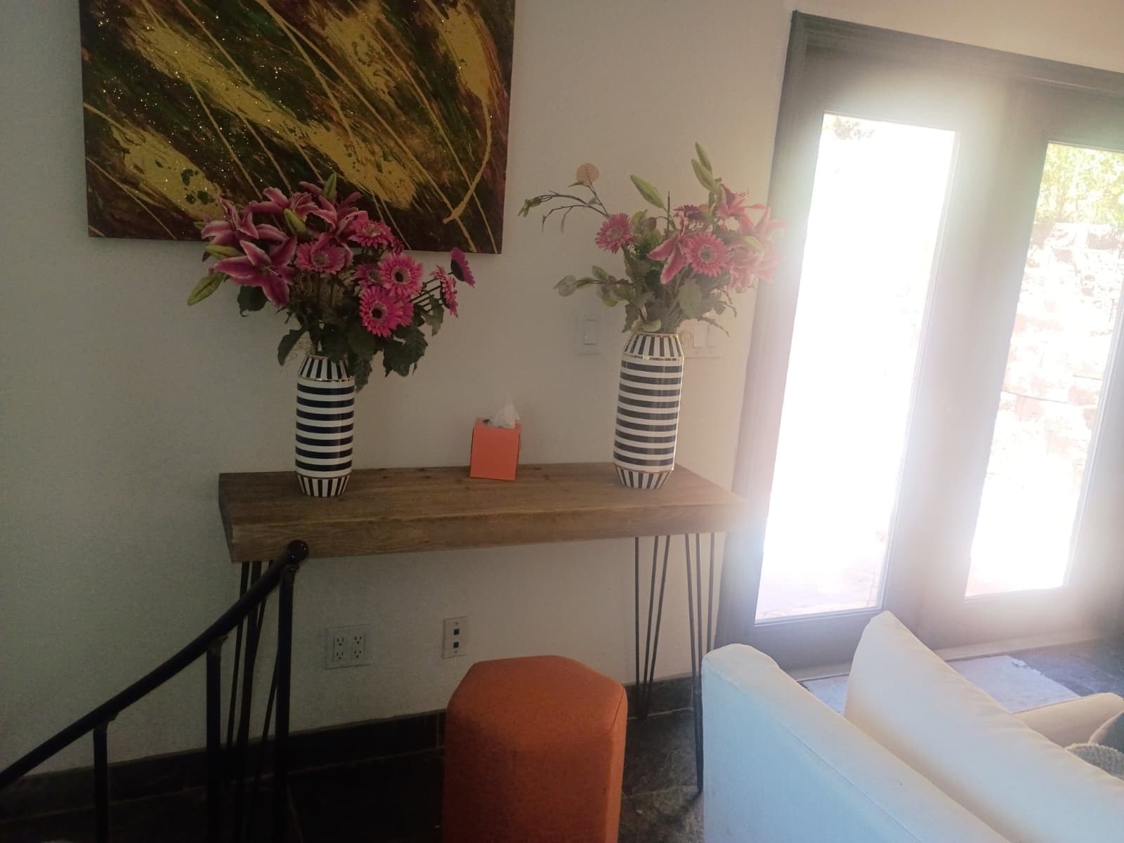 Ein Zimmer mit einem Holzkonsolentisch, auf dem zwei gestreifte Vasen mit Blumen stehen, einem Gemälde darüber und einem weißen Sofa.