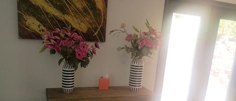 Una habitación con una consola de madera que sostiene dos jarrones a rayas con flores, un cuadro en la pared y un sofá blanco.