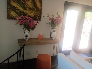 Quarto com mesa de consola de madeira, dois vasos listrados com flores, um quadro acima e um sofá branco.