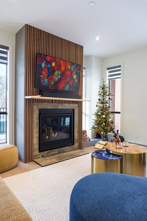 Ein modernes Wohnzimmer mit Kamin, einem an einer Holzplatte montierten Flachbildfernseher, einem Weihnachtsbaum und einem runden Couchtisch.
