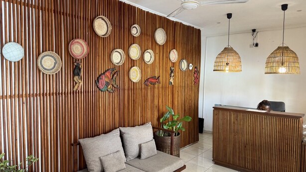 A reception area with a wooden slat wall, woven wall hangings, a sofa, a reception desk, and two hanging pendant lights.