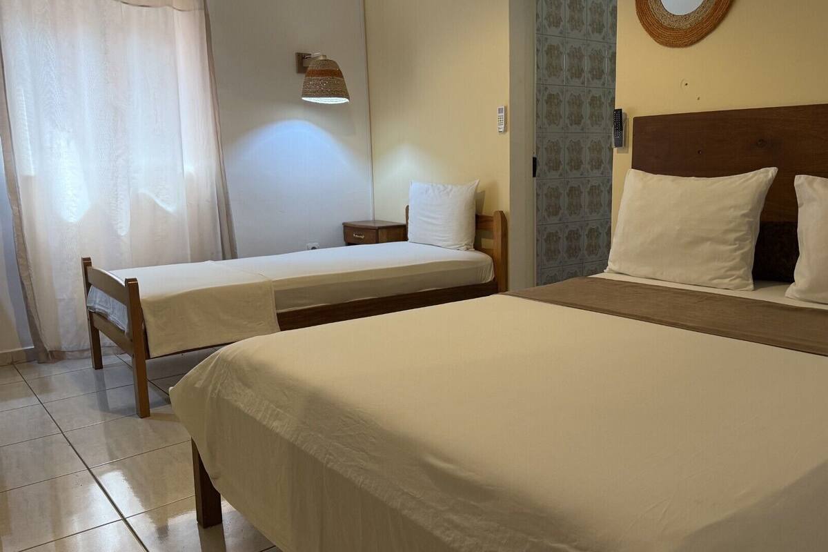 A hotel room with two single beds, a nightstand, a lamp, a wall-mounted phone, and a decorative wall hanging.