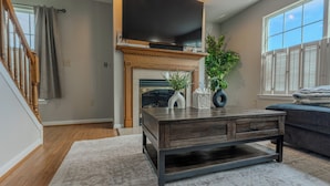 Een woonkamer met een open haard, een flatscreen televisie erboven, een salontafel en een bank.