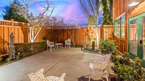 Une terrasse à l’arrière de la maison, avec une clôture en bois, du mobilier d’extérieur et une porte verte.