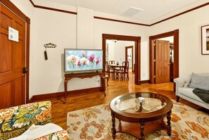 A living room with a television, a sofa, a coffee table, and a dining area in the background.