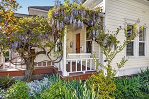 Une maison avec un porche, un arbre aux fleurs violettes et une variété de plantes.