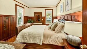 A bedroom with a large bed, wooden headboard, a nightstand, a mirror, and framed artwork on the walls. - Whimsy on B | 2BR Steps to Downtown (Ashland)