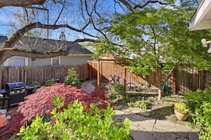Un jardin avec une clôture en bois, un barbecue, un vélo et diverses plantes.