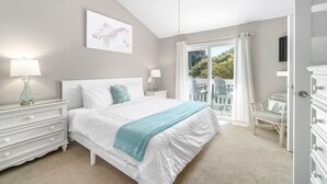 Ein Schlafzimmer mit Bett, Nachttischen, Deckenventilator, einem Fenster mit Vorhängen und Blick ins Freie.