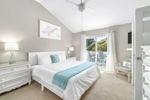 Une chambre à coucher comprenant un lit, des tables de chevet, un ventilateur de plafond, une fenêtre avec des rideaux et une vue sur l’extérieur.