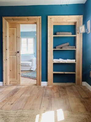 Ein Zimmer mit Holzboden, einer blauen Wand und einer eingebauten Holzregaleinrichtung mit gefalteten Decken.