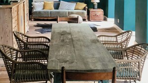 Ein Zimmer mit einem Holztisch, Korbstühlen, einer Couch und einer Pendelleuchte.