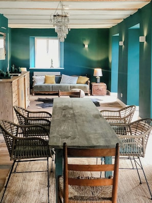 Ein Zimmer mit einem Holztisch, Korbstühlen, einer Couch und einer Pendelleuchte.