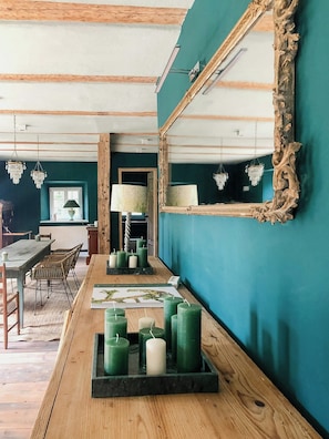 Ein Zimmer mit türkisfarbenen Wänden, einem Holztisch mit Kerzen, einem Spiegel mit aufwendigem Rahmen und einer Kristallleuchter.
