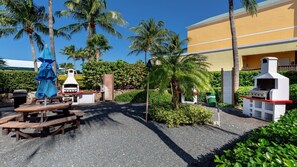 Un espace extérieur aménagé en terrasse, avec des barbecues, des tables de pique-nique et des palmiers.