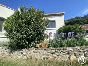 Una casa con un muro in pietra, un grande cespuglio e fiori viola nel giardino.